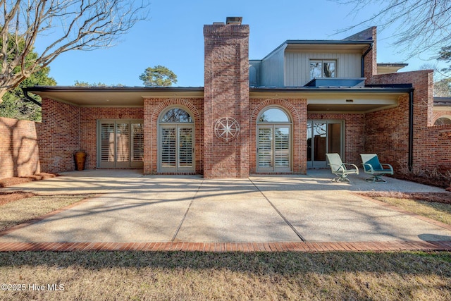 rear view of property with brick siding, french doors, a chimney, and a patio