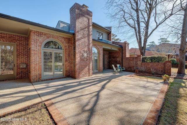 rear view of property with brick siding, a chimney, and a patio area