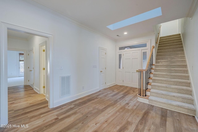 foyer featuring visible vents, crown molding, stairs, light wood-style flooring, and a skylight