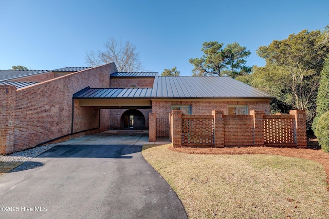 exterior space with brick siding, aphalt driveway, a front yard, metal roof, and a standing seam roof