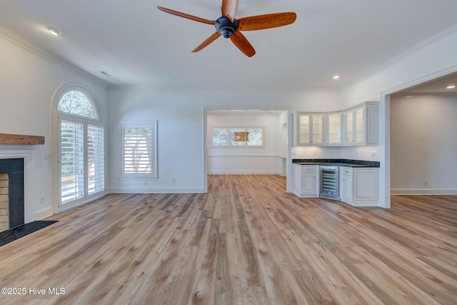 unfurnished living room with wine cooler, light wood-style flooring, crown molding, and a ceiling fan