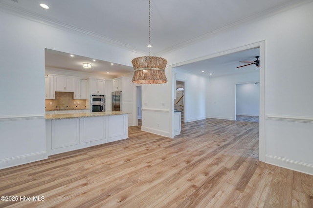 kitchen with light wood finished floors, white cabinets, open floor plan, appliances with stainless steel finishes, and tasteful backsplash