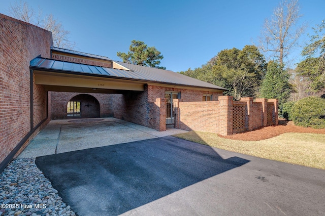 exterior space with a standing seam roof, aphalt driveway, fence, metal roof, and brick siding