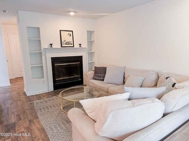 living room with baseboards, built in features, wood finished floors, a glass covered fireplace, and a textured ceiling