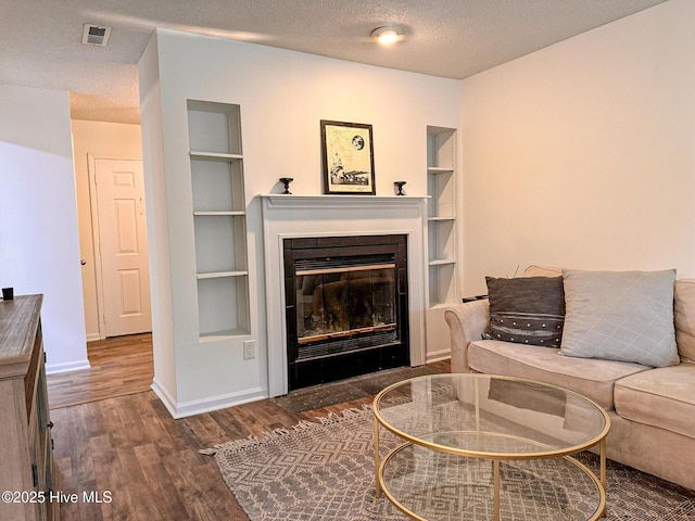 living room with visible vents, built in features, a textured ceiling, wood finished floors, and baseboards