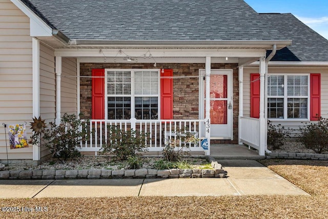 view of exterior entry with stone siding, a porch, and a shingled roof