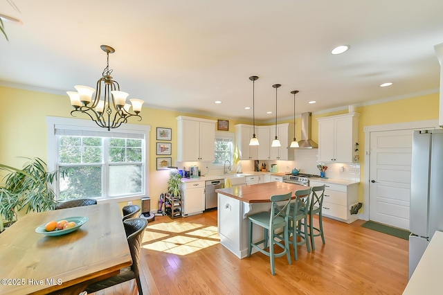 kitchen with light wood-type flooring, stainless steel appliances, ornamental molding, and wall chimney range hood