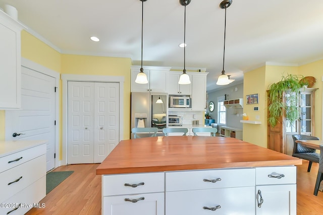 kitchen with decorative light fixtures, stainless steel appliances, light wood-type flooring, and white cabinetry