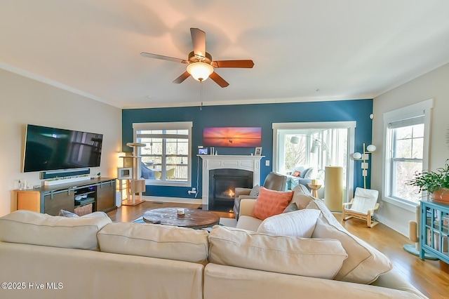 living area with ceiling fan, baseboards, a fireplace with flush hearth, and wood finished floors