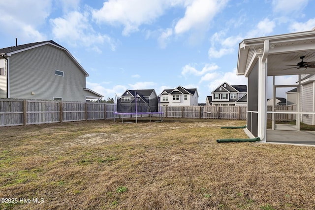 view of yard with a trampoline, a fenced backyard, a residential view, and ceiling fan