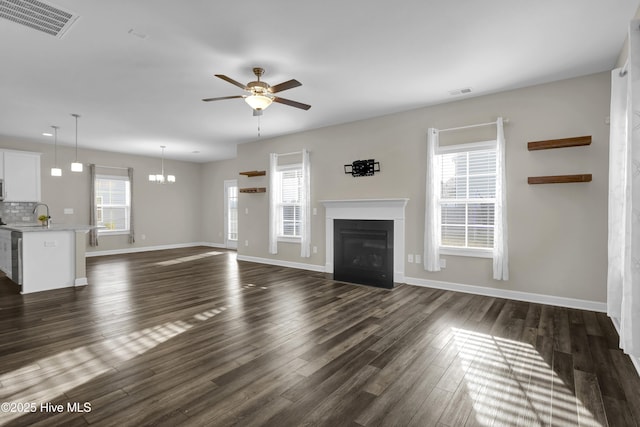 unfurnished living room featuring ceiling fan with notable chandelier, visible vents, dark wood-style flooring, and a healthy amount of sunlight