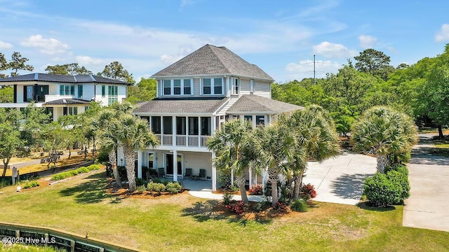 back of property with a sunroom, a shingled roof, and a lawn