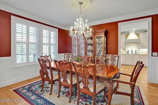dining space with an inviting chandelier, plenty of natural light, a wainscoted wall, and light wood-style floors