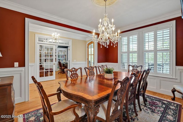 dining space featuring light wood-style floors, an inviting chandelier, a decorative wall, and a wainscoted wall