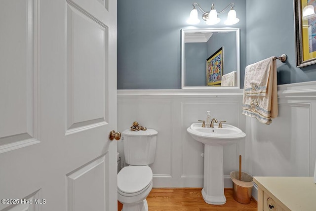 bathroom featuring a wainscoted wall, toilet, a decorative wall, and wood finished floors