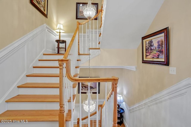 stairs with a notable chandelier, a decorative wall, and a wainscoted wall