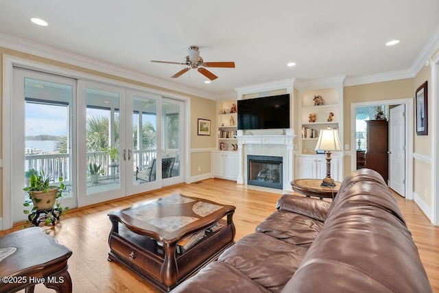 living room with light wood finished floors, french doors, a fireplace with flush hearth, ceiling fan, and ornamental molding