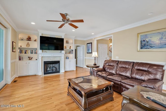 living area featuring ornamental molding, light wood-type flooring, visible vents, ceiling fan, and a fireplace with flush hearth