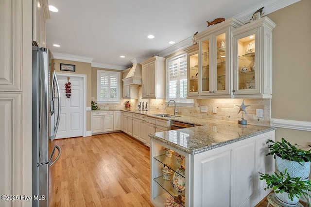 kitchen featuring freestanding refrigerator, ornamental molding, a healthy amount of sunlight, a sink, and custom range hood