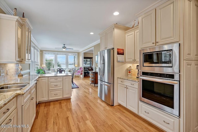 kitchen featuring a peninsula, appliances with stainless steel finishes, crown molding, open floor plan, and light wood-style floors