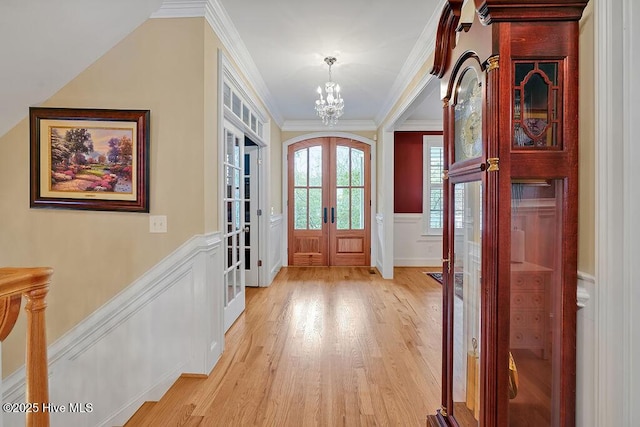 entrance foyer featuring french doors, ornamental molding, a decorative wall, a chandelier, and light wood-type flooring