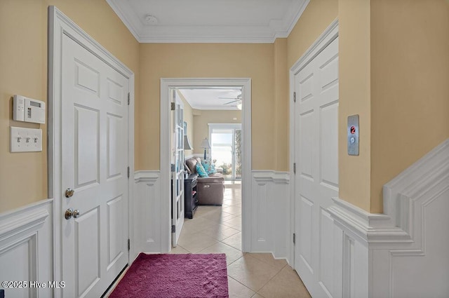 corridor featuring wainscoting, crown molding, light tile patterned flooring, and a decorative wall
