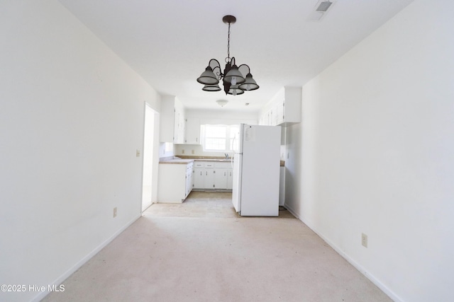 kitchen with a notable chandelier, white cabinets, concrete flooring, and freestanding refrigerator