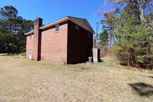 view of property exterior featuring brick siding, central AC, a chimney, and a yard