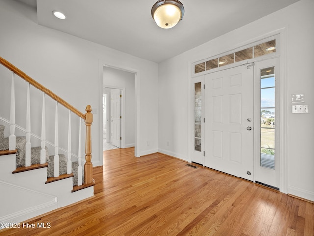 entryway with light wood finished floors, visible vents, stairs, and baseboards