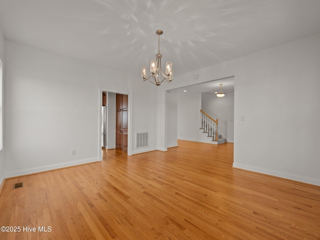 spare room with a chandelier, visible vents, light wood-type flooring, and baseboards