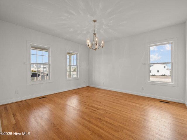 spare room featuring light wood-style floors, visible vents, baseboards, and a notable chandelier