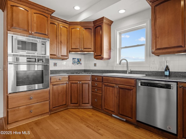 kitchen with brown cabinets, a sink, dark countertops, appliances with stainless steel finishes, and light wood finished floors