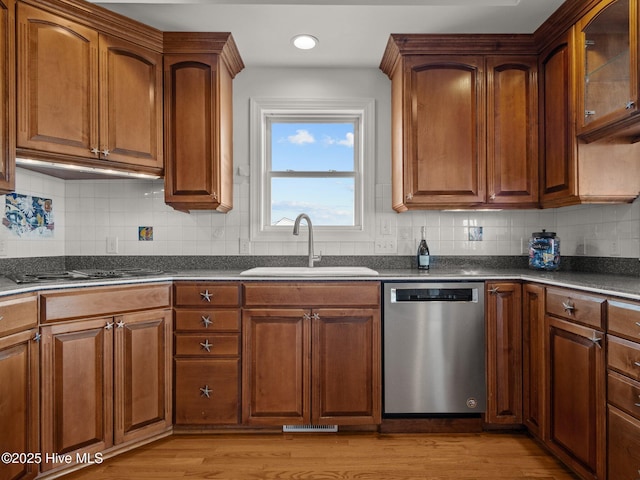 kitchen featuring stainless steel dishwasher, dark countertops, stovetop, and a sink