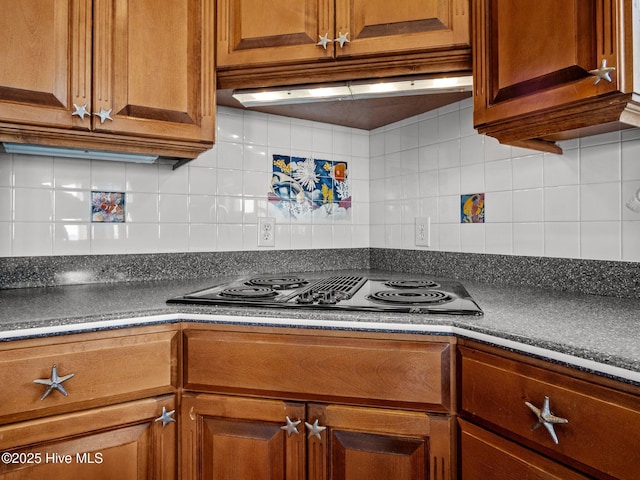 kitchen with dark countertops, stovetop with downdraft, brown cabinets, and decorative backsplash