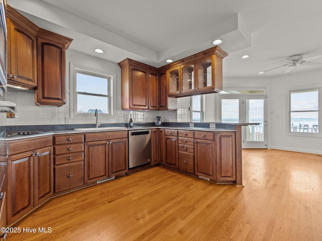 kitchen featuring light wood-type flooring, a sink, stainless steel dishwasher, dark countertops, and a peninsula