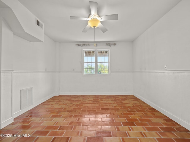 empty room with a wainscoted wall, a ceiling fan, and visible vents