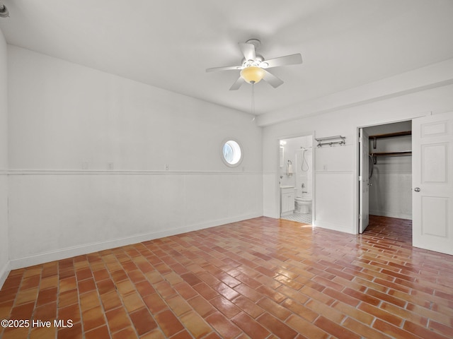 unfurnished bedroom featuring a closet, a ceiling fan, ensuite bathroom, and brick floor