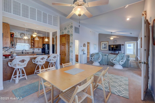 dining space featuring light colored carpet, a ceiling fan, visible vents, and high vaulted ceiling