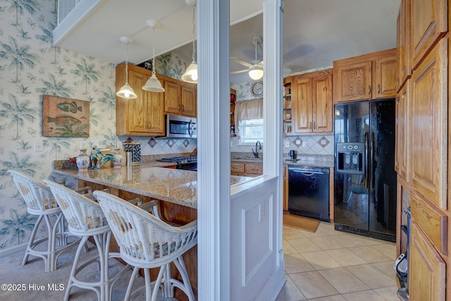 kitchen with black appliances, a kitchen breakfast bar, wallpapered walls, light tile patterned floors, and light stone countertops