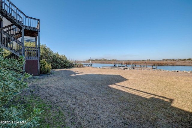 view of yard featuring stairs, a water view, and a boat dock