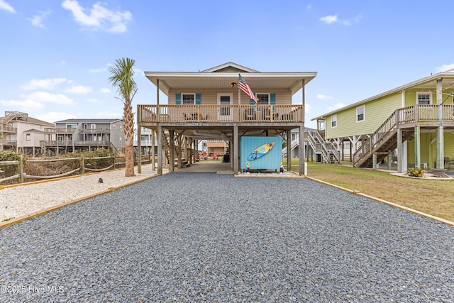 coastal home with a front lawn, stairway, gravel driveway, covered porch, and a carport