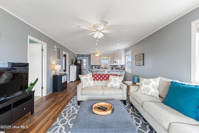 living area featuring dark wood-type flooring, a ceiling fan, and ornamental molding