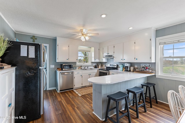 kitchen with under cabinet range hood, dark wood finished floors, a peninsula, white cabinets, and stainless steel appliances