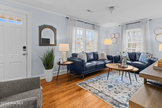 living room with light wood-style flooring, crown molding, baseboards, and visible vents