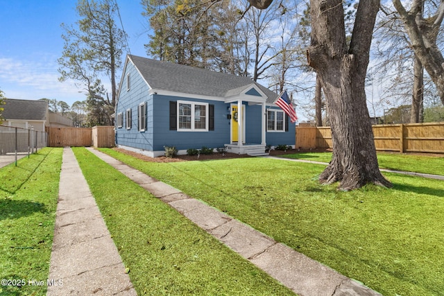 bungalow-style home with roof with shingles, a front yard, driveway, and fence