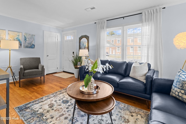 living area with wood finished floors, ornamental molding, baseboards, and visible vents