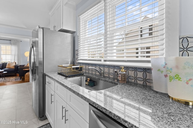 kitchen with decorative backsplash, white cabinets, a sink, light stone counters, and freestanding refrigerator