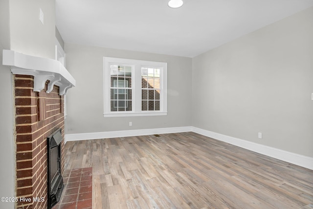 unfurnished living room with a fireplace, baseboards, and wood finished floors