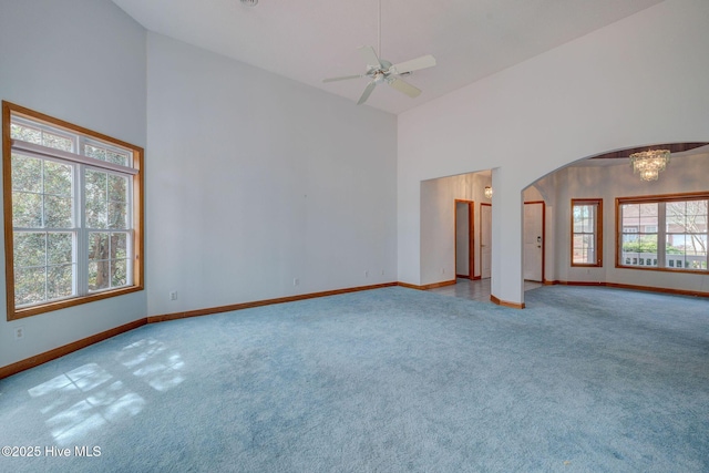 carpeted spare room featuring arched walkways, ceiling fan with notable chandelier, high vaulted ceiling, and baseboards