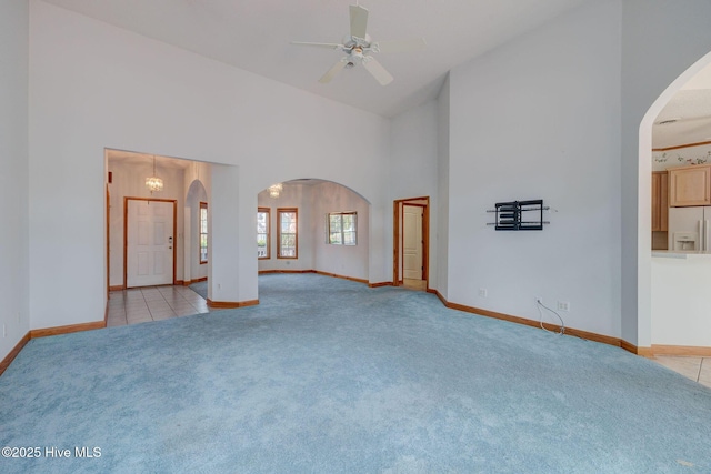 unfurnished room with baseboards, ceiling fan, carpet flooring, arched walkways, and high vaulted ceiling